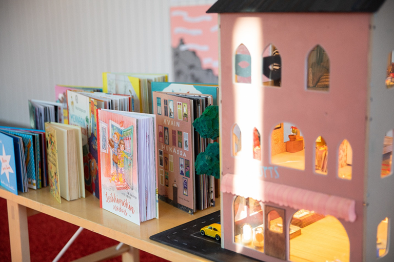 Kuvassa on pöydällä kirjoja sekä pieni talo.