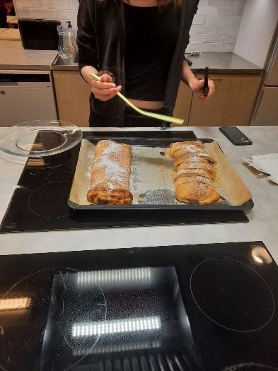 Opiskelija seisoo lieden edessä kotitaloustunnilla. Liedellä on pelti ja lieden vieressä tarjoiluastia, jolle opiskelija laittaa pellillä olevat leivonnaiset tarjolle.