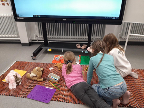 Kuvassa on lapsia leikkimässä matolla luokkahuoneessa